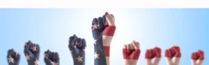 Raised fists painted with the American flag and stars and stripes, symbolizing unity or protest, against a light blue background.